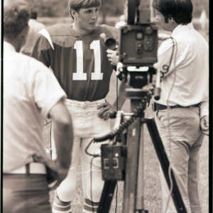 Football player and interviewers at practice, 1973