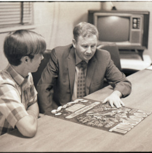 Coach Norm Sloan and other looking at football poster, circa 1970