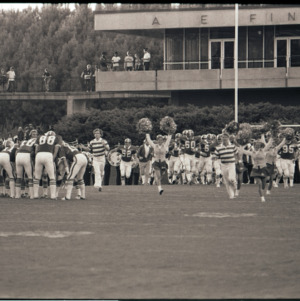 Football players and cheerleaders on field, circa 1969-1975
