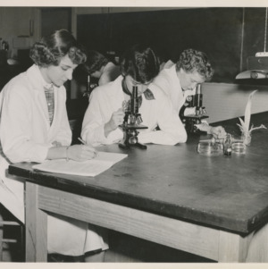 Women students looking through microscopes and taking notes in the lab