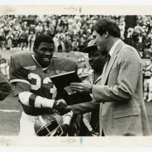 NC State football player 23 accepts a plaque from the coach