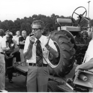 Man on intercom with group in front of tractor