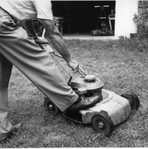 Lawn mower safety demonstration photograph showing the correct way to start a power lawn mower