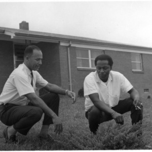 Two unidentified men crouching in front of a house