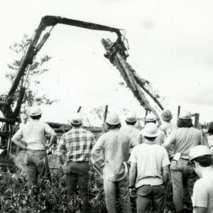 Men in hardhats in field watching excavating machine