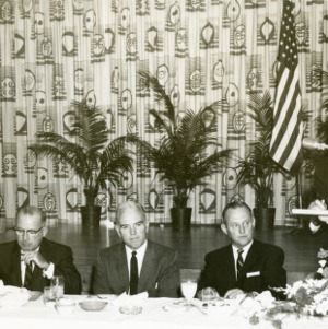 Man speaking at podium with four other men seated