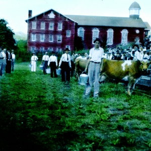 Men with cows and milk buckets between stands of people in front of a church