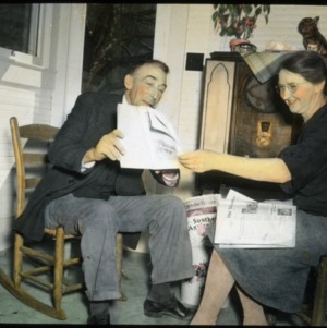 Man and woman sitting in front of a radio looking at a publication