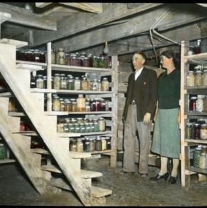Man and woman standing in cellar full of canned goods