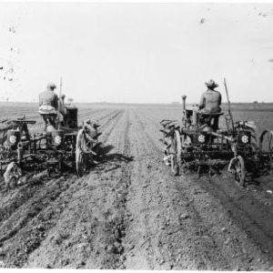 Two workers tilling field with tractors