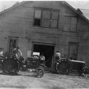 Men and three tractors in front of barn